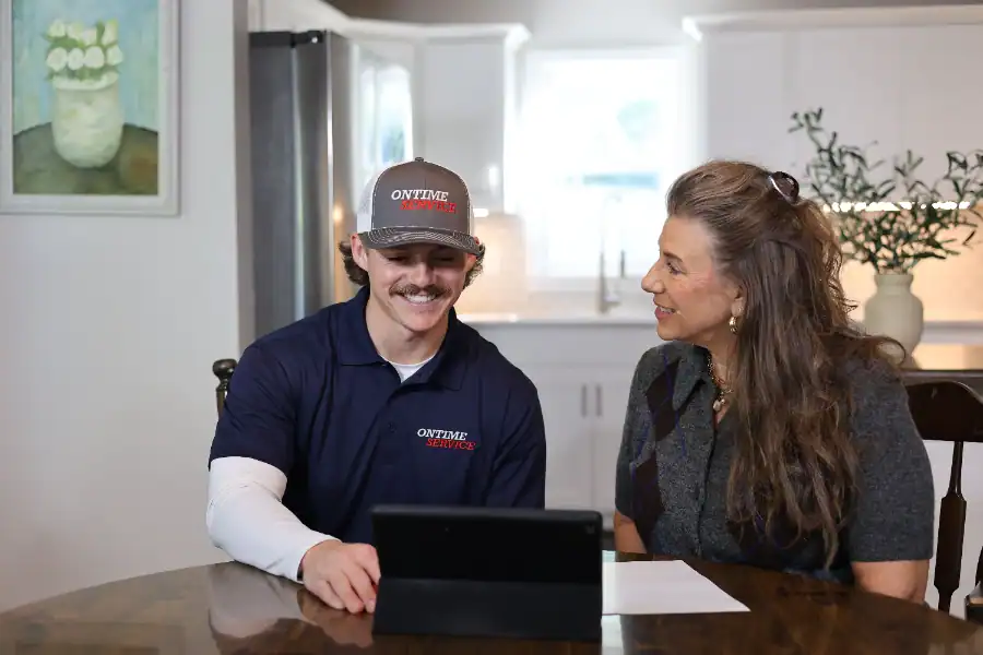 A man in a company uniform and a woman sit at a kitchen table, looking at a tablet together with papers nearby.